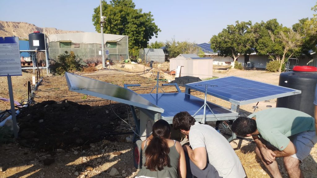 שני צעירים עם הגב למצלמה בוחנים ניסוי בפאנלים סולארים, חוץ, אור יום